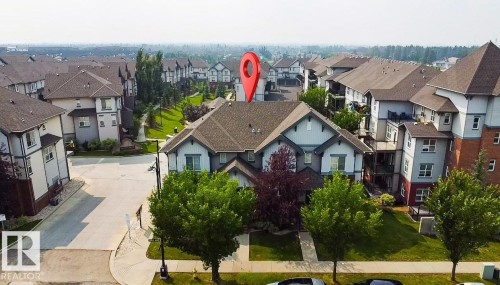 Multi-level residential building featuring a gabled roofline, light-toned siding, and surrounding green spaces - #62 675 Watt Bv Sw, Edmonton, AB - Outdoor With Facade