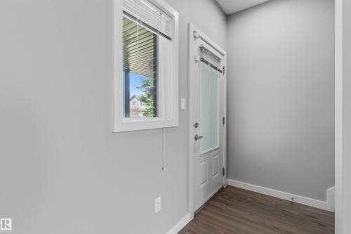 Entryway featuring a white paneled door with frosted glass, a single window with blinds, light gray walls, and wood-finish flooring - #62 675 Watt Bv Sw, Edmonton, AB - Indoor Photo Showing Other Room