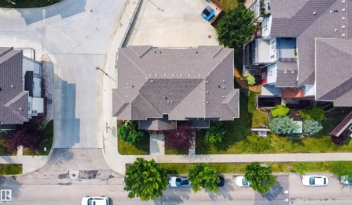 Aerial perspective highlighting the property with a gray shingle roof, green lawn, mature trees, and a concrete driveway - #62 675 Watt Bv Sw, Edmonton, AB - Outdoor