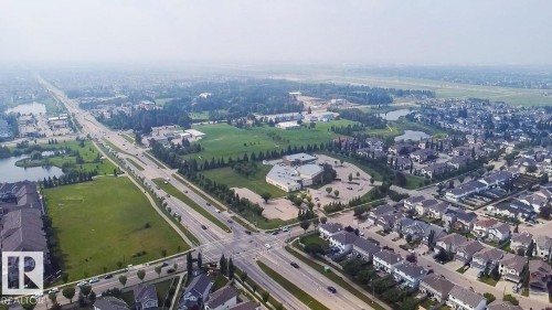 Aerial perspective of a developed residential area featuring multiple housing styles, extensive green spaces, and a prominent intersection - #62 675 Watt Bv Sw, Edmonton, AB - Outdoor With View
