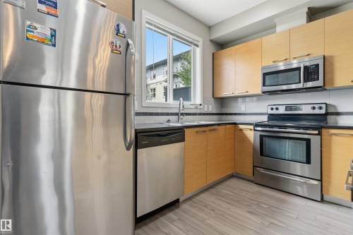 Modern kitchen featuring wood-finish cabinetry, stainless steel appliances, dark countertops, and a subway tile backsplash with accent trim - #62 675 Watt Bv Sw, Edmonton, AB - Indoor Photo Showing Kitchen