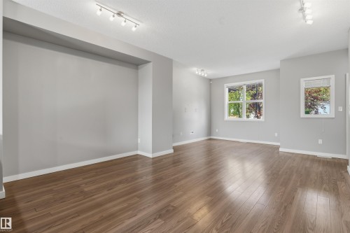 Spacious room featuring wood-finish flooring, light gray walls, white baseboards, and multiple windows - #62 675 Watt Bv Sw, Edmonton, AB - Indoor