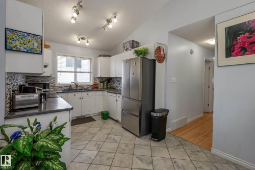 Kitchen featuring white cabinetry, dark countertops, a mosaic tile backsplash, a stainless steel refrigerator, and track lighting - 9113 166 Avenue Nw, Edmonton, AB - Indoor Photo Showing Kitchen With Double Sink