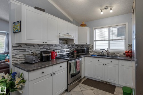Kitchen featuring white cabinetry, gray countertops, and a mosaic tile backsplash - 9113 166 Avenue Nw, Edmonton, AB - Indoor Photo Showing Kitchen With Double Sink