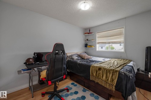 Bedroom featuring light-toned walls, wood-finish flooring, a window with blinds, and a ceiling-mounted light fixture - 9113 166 Avenue Nw, Edmonton, AB - Indoor Photo Showing Bedroom