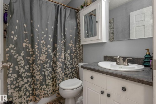 Bathroom vanity featuring a white cabinet with dark hardware, a dark countertop, and an oval undermount sink with a brushed nickel faucet - 9113 166 Avenue Nw, Edmonton, AB - Indoor Photo Showing Bathroom