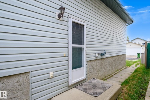 Light-colored horizontal siding exterior featuring a storm door, concrete step, and wall-mounted exterior light fixture - 9113 166 Avenue Nw, Edmonton, AB - Outdoor With Exterior