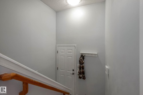 Stairwell entrance featuring a paneled door, high ceilings, and a wooden handrail with white trim - 9113 166 Avenue Nw, Edmonton, AB - Indoor Photo Showing Other Room