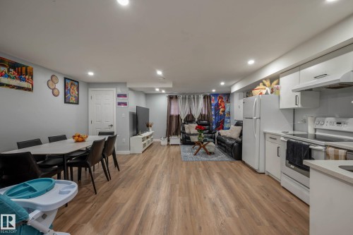 Open-concept living space featuring wood-finish flooring throughout, recessed lighting, and a contemporary kitchen with white cabinetry, white appliances, and a light-toned countertop - 9113 166 Avenue Nw, Edmonton, AB - Indoor