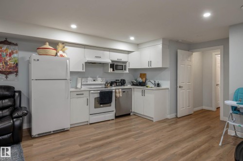 Open-concept kitchen area featuring wood-finish flooring, white cabinetry, a built-in stainless steel dishwasher, and a white oven - 9113 166 Avenue Nw, Edmonton, AB - Indoor Photo Showing Kitchen