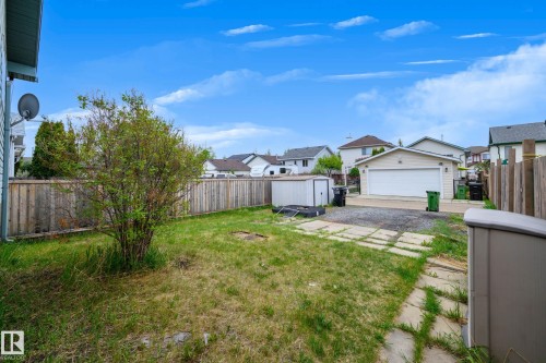 Expansive backyard featuring a detached garage, wood privacy fencing, a storage shed, and concrete patio stones - 9113 166 Avenue Nw, Edmonton, AB - Outdoor
