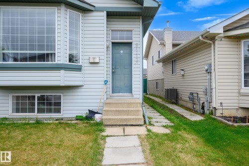 Light-toned siding exterior featuring a bay window, concrete steps, and a complementary blue entry door - 9113 166 Avenue Nw, Edmonton, AB - Outdoor With Exterior