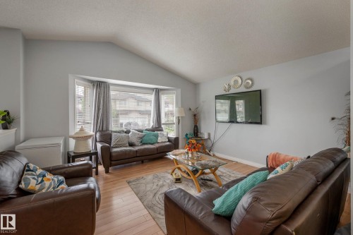 Living area featuring a vaulted ceiling, wood-finish flooring, bay window with blinds, and light gray wall paint - 9113 166 Avenue Nw, Edmonton, AB - Indoor Photo Showing Living Room