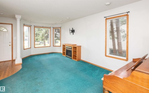 Bright living space featuring a bay window, wood-finish flooring, and an electric fireplace with built-in shelving - 5116 51 Avenue, Pickardville, AB - Indoor Photo Showing Other Room