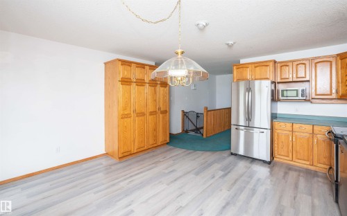 Kitchen and dining area featuring light wood-finish flooring, oak cabinetry, stainless steel refrigerator, and a built-in microwave - 5116 51 Avenue, Pickardville, AB - Indoor Photo Showing Kitchen