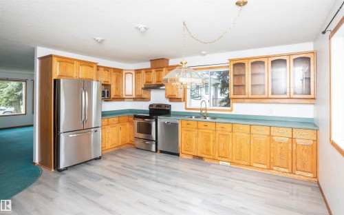 Kitchen featuring light wood-finish cabinetry with glass-front uppers, stainless steel appliances, a double basin sink, and wood-finish flooring - 5116 51 Avenue, Pickardville, AB - Indoor Photo Showing Kitchen