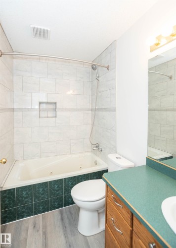 Bathroom featuring a jetted tub with white tile surround, a built-in shower niche, and a vanity with a green countertop and wood cabinetry - 5116 51 Avenue, Pickardville, AB - Indoor Photo Showing Bathroom