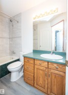 Bathroom featuring a wood-finish vanity with a built-in sink and countertop, a wall-mounted mirror with integrated lighting, a tub/shower combination with tile surround, and wood-finish flooring - 