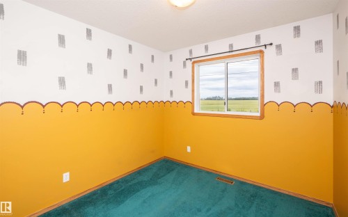 Interior room featuring a window with a wood-finish frame, teal carpeting, and a two-tone painted wall with an orange lower section and a white upper section with a patterned design - 5116 51 Avenue, Pickardville, AB - Indoor Photo Showing Other Room