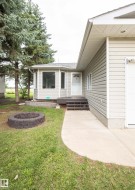 Exterior featuring light-colored horizontal siding, a bay window with white trim, and mature evergreen trees - 