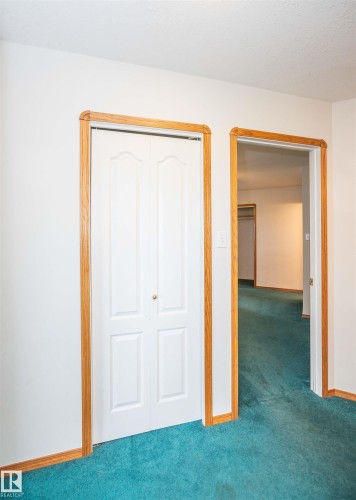 Interior space featuring a white bi-fold closet door with a brass-toned knob, light wood door frames, and bright turquoise carpeting - 5116 51 Avenue, Pickardville, AB - Indoor