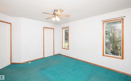 Spacious room featuring a ceiling fan with integrated lighting, wood-trimmed windows, and a vibrant teal carpet - 5116 51 Avenue, Pickardville, AB - Indoor Photo Showing Other Room