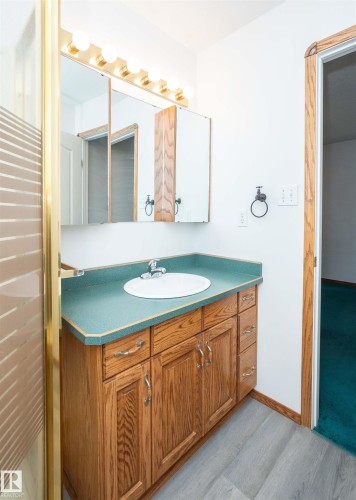 Bathroom vanity featuring a wood-finish cabinet with chrome hardware, an integrated sink, and a contrasting countertop - 5116 51 Avenue, Pickardville, AB - Indoor Photo Showing Bathroom