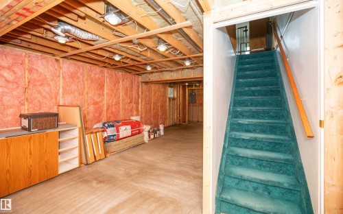 Unfinished basement with exposed wood framing and concrete flooring, featuring a built-in wood-finish cabinet, recessed lighting, and a carpeted staircase with a wood handrail - 5116 51 Avenue, Pickardville, AB - Indoor