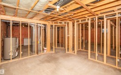 Unfinished basement featuring wood framing for multiple rooms, exposed ceiling joists with insulation, a water heater, and concrete flooring - 