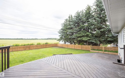 Expansive backyard featuring a multi-level composite deck, wooden privacy fence, mature evergreen trees, and a manicured lawn backing onto open fields - 5116 51 Avenue, Pickardville, AB - Outdoor With Deck Patio Veranda