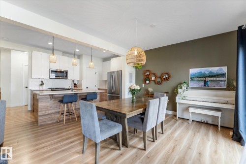 Open-concept living area featuring light wood-finish flooring, a contemporary dining table, and a kitchen with white cabinetry - 6875 Evans Wynd Nw, Edmonton, AB - Indoor Photo Showing Dining Room