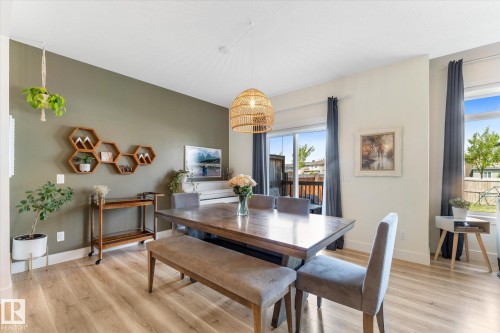 Open-concept dining area featuring wood-finish flooring, a contemporary woven pendant light fixture, and a sliding glass patio door - 6875 Evans Wynd Nw, Edmonton, AB - Indoor Photo Showing Dining Room