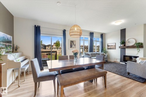 Open-concept living area with wood-finish flooring, a contemporary fireplace feature, and a sliding glass door to an outdoor deck - 6875 Evans Wynd Nw, Edmonton, AB - Indoor