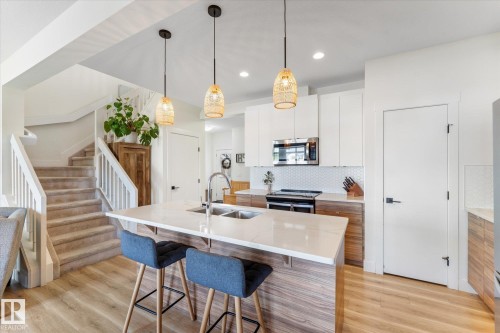 Modern kitchen featuring a large island with dual sinks, quartz countertops, and contemporary pendant lighting - 6875 Evans Wynd Nw, Edmonton, AB - Indoor Photo Showing Kitchen With Double Sink With Upgraded Kitchen