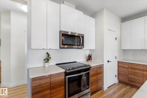 Contemporary kitchen featuring white upper cabinetry, rich wood-finish lower cabinetry, white honeycomb tile backsplash, and light-toned countertops - 6875 Evans Wynd Nw, Edmonton, AB - Indoor Photo Showing Kitchen