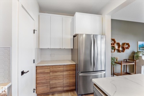 Kitchen featuring a stainless steel refrigerator, white upper cabinetry, and wood-finish lower cabinetry - 6875 Evans Wynd Nw, Edmonton, AB - Indoor Photo Showing Kitchen