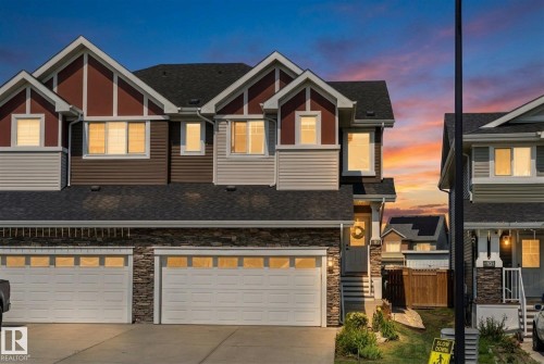 Contemporary townhome with a dark shingle roof, two-car garage, stacked stone facade, and multi-toned siding accents - 6875 Evans Wynd Nw, Edmonton, AB - Outdoor With Facade