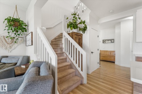 Staircase with white balusters and carpeted treads, complemented by light wood-finish flooring - 6875 Evans Wynd Nw, Edmonton, AB - Indoor Photo Showing Other Room