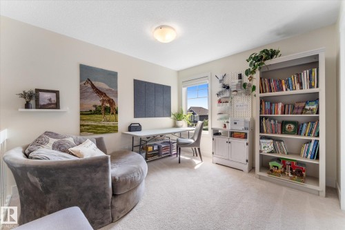 Bright room featuring light-toned carpeting, a window with exterior views, built-in shelving, a built-in cabinet, and a flush-mount ceiling light fixture - 6875 Evans Wynd Nw, Edmonton, AB - Indoor