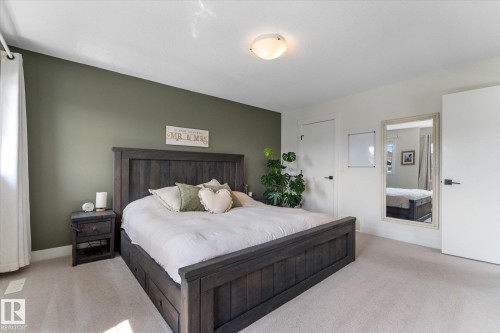 Carpeted bedroom featuring a dark-stained wood bed frame with storage drawers, a complementary nightstand, a prominent accent wall, and a full-length mirror - 6875 Evans Wynd Nw, Edmonton, AB - Indoor Photo Showing Bedroom