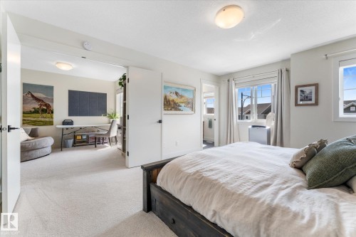 Carpeted bedroom with a dark wood-finish bed frame, multiple windows, and a doorway opening to a secondary room - 6875 Evans Wynd Nw, Edmonton, AB - Indoor Photo Showing Bedroom