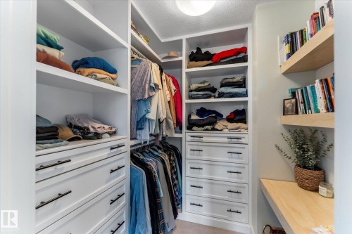 Custom closet system featuring built-in white cabinetry, integrated shelving, and multiple hanging rods - 6875 Evans Wynd Nw, Edmonton, AB - Indoor With Storage