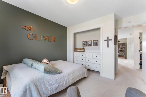 Bedroom featuring a contrasting accent wall, built-in recessed shelving, light-toned carpeting, and a flush-mount ceiling light fixture - 6875 Evans Wynd Nw, Edmonton, AB - Indoor Photo Showing Bedroom