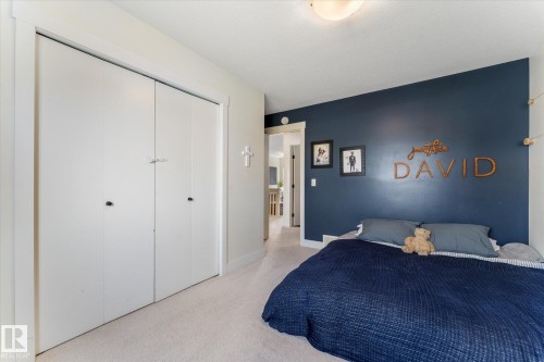 Bedroom featuring a deep blue accent wall, neutral carpeting, white trim, and a bi-fold closet with white doors - 6875 Evans Wynd Nw, Edmonton, AB - Indoor Photo Showing Bedroom
