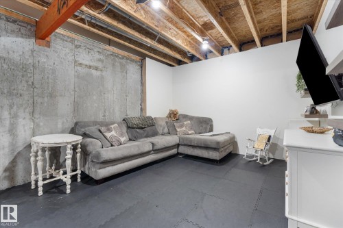 Unfinished basement space featuring exposed concrete walls, exposed wooden ceiling joists, and a partial finished wall with a wall-mounted display - 6875 Evans Wynd Nw, Edmonton, AB - Indoor Photo Showing Basement
