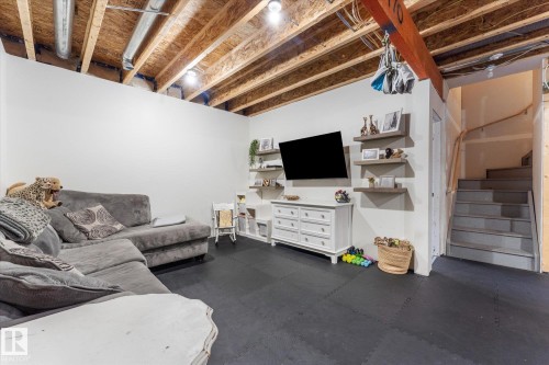 Finished lower level featuring exposed ceiling joists, recessed lighting, wall-mounted display shelving, and black interlocking floor tiles - 6875 Evans Wynd Nw, Edmonton, AB - Indoor Photo Showing Basement