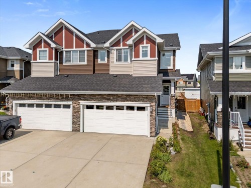 Multi-level residential exterior featuring a two-car garage with stone facade - 6875 Evans Wynd Nw, Edmonton, AB - Outdoor With Facade