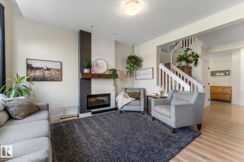 Living area featuring a contemporary fireplace with a dark accent wall and a rustic wood mantel - 6875 Evans Wynd Nw, Edmonton, AB - Indoor Photo Showing Living Room With Fireplace