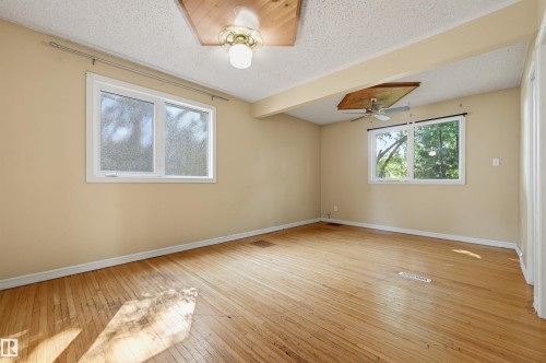 Spacious room featuring wood-finish flooring, two windows, and a ceiling fan - 7754 80 Avenue Nw, Edmonton, AB - Indoor Photo Showing Other Room