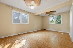 Spacious room featuring wood-finish flooring, two windows, and a ceiling fan - 